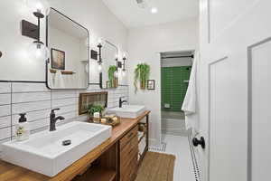 Bathroom with double vanity, washtub / shower combination, decorative backsplash, and tile patterned floors