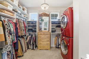 Walk in closet featuring light colored carpet, estacked washer and dryer, and a chandelier