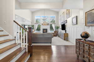 Living room with a glass covered fireplace, dark wood-style flooring, stairs, a chandelier, and wainscoting