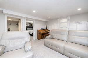 Carpeted living area featuring a decorative wall, a textured ceiling, recessed lighting, and a wainscoted wall