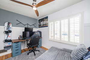 Home office featuring wood finished floors, a textured ceiling, a wainscoted wall, and a ceiling fan