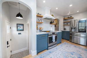 Kitchen with arched walkways, stainless steel appliances, premium range hood, a textured ceiling, and light wood-type flooring