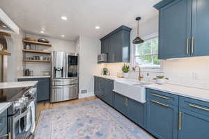 Kitchen featuring blue cabinetry, stainless steel appliances, light wood-style flooring, backsplash, and recessed lighting