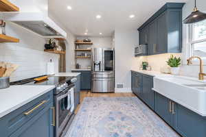 Kitchen with blue cabinetry, stainless steel appliances, backsplash, wall chimney exhaust hood, and a textured ceiling