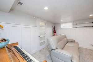 Living room with a textured ceiling, a decorative wall, a wainscoted wall, carpet, and recessed lighting