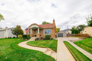 View of front facade with a chimney, brick siding, an outbuilding, and a tile roof