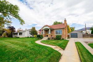 View of front of house featuring a chimney, brick siding, an outdoor structure, driveway, and a garage