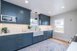 Kitchen featuring blue cabinetry, light wood-style floors, pendant lighting, a textured ceiling, and appliances with stainless steel finishes