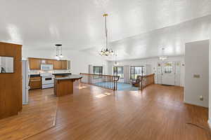 Kitchen featuring a textured ceiling, brown cabinetry, decorative light fixtures, lofted ceiling, and white appliances