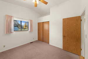 Unfurnished bedroom featuring vaulted ceiling, carpet, a closet, and ceiling fan