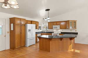 Kitchen with a chandelier, brown cabinetry, a kitchen bar, white appliances, and vaulted ceiling
