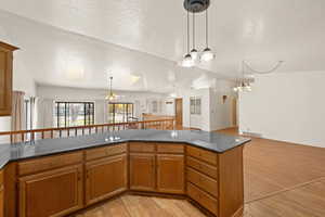 Kitchen with brown cabinetry, a textured ceiling, open floor plan, light wood-type flooring, and dark stone counters