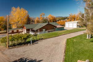View of front of property with a garage, a porch, an outbuilding, driveway, and view of wooded area