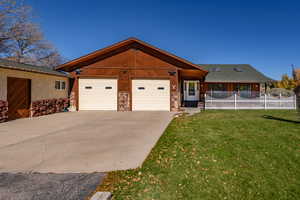 View of front of home featuring stone siding, a front lawn, concrete driveway, and an attached garage