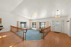 Entrance foyer featuring a textured ceiling, a chandelier, vaulted ceiling, light wood finished floors, and ceiling fan