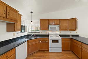 Kitchen featuring brown cabinetry, white appliances, hanging light fixtures, light wood-type flooring, and a textured ceiling