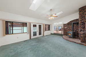 Unfurnished living room with a wood stove, lofted ceiling, a skylight, carpet floors, and french doors