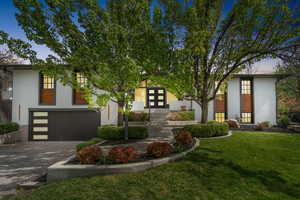 View of front of home with decorative driveway, a front yard, a garage, brick siding, and french doors