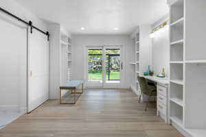 Office space with a barn door, built in desk, light wood-style floors, recessed lighting, and built in features