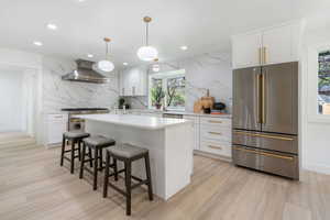Kitchen featuring premium appliances, white cabinets, a breakfast bar, hanging light fixtures, and backsplash