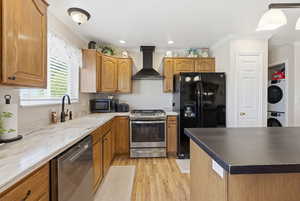 Kitchen featuring black appliances, crown molding, wall chimney exhaust hood, light wood-type flooring, and brown cabinetry