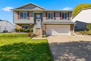 Bi-level home featuring brick siding, driveway, a garage, and a front lawn