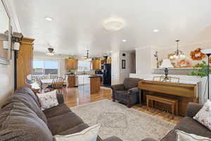 Living room with light wood-style flooring, a chandelier, ornamental molding, and recessed lighting