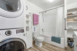 Bathroom with wood tiled floors, shower / tub combo with curtain, and estacked washer and dryer