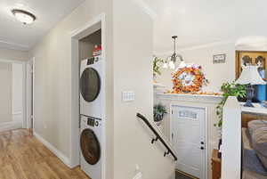 Laundry room with light wood finished floors, estacked washer and dryer, ornamental molding, a textured ceiling, and a chandelier