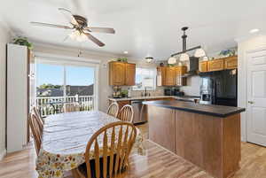 Kitchen with black appliances, ornamental molding, light wood-type flooring, a center island, and wall chimney exhaust hood
