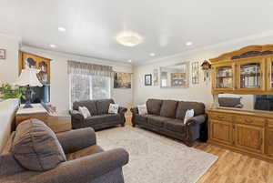 Living room featuring light wood-type flooring, crown molding, and recessed lighting