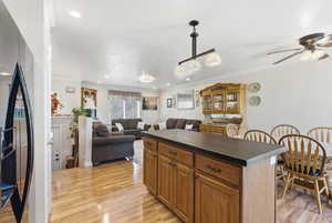 Kitchen featuring dark countertops, a kitchen island, brown cabinetry, stainless steel fridge with ice dispenser, and light wood-style flooring