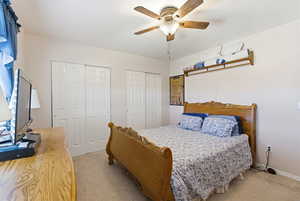Bedroom featuring two closets, light carpet, and a ceiling fan