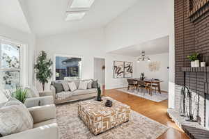 Living area with wood finished floors, plenty of natural light, a brick fireplace, high vaulted ceiling, and a skylight