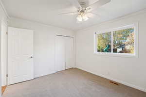 Unfurnished bedroom featuring light colored carpet, a closet, a ceiling fan, and crown molding