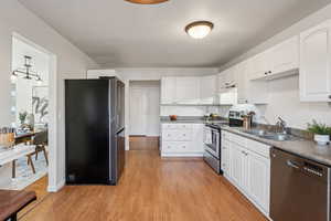 Kitchen featuring appliances with stainless steel finishes, white cabinetry, light wood-style floors, and dark countertops