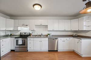 Kitchen featuring stainless steel appliances, white cabinetry, dark countertops, and light wood-style flooring
