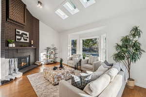Living room with a skylight, high vaulted ceiling, wood finished floors, and a fireplace