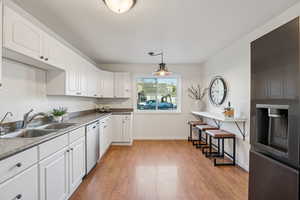 Kitchen with refrigerator with ice dispenser, white cabinets, light wood-style floors, stainless steel dishwasher, and a kitchen bar