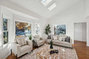 Living room featuring a skylight, high vaulted ceiling, and wood finished floors
