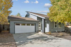 View of front of house with an attached garage, concrete driveway, and a shingled roof