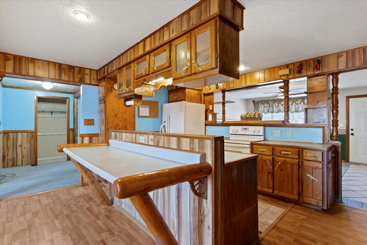 Kitchen featuring wooden walls, brown cabinetry, white appliances, light wood-style flooring, and a wainscoted wall