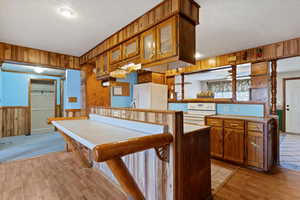 Kitchen featuring wooden walls, brown cabinetry, white appliances, light wood-style flooring, and a wainscoted wall