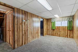 Below grade area featuring a drop ceiling, carpet floors, and wooden walls