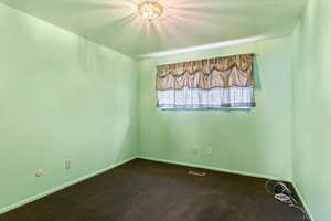 Unfurnished room with dark carpet and baseboards