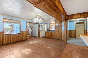 Foyer with wooden walls, wainscoting, light wood-style flooring, stairs, and a textured ceiling