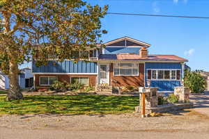 Split level home featuring board and batten siding, a metal roof, brick siding, and a front lawn