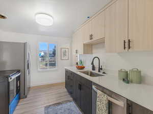 Kitchen with light stone counters, light wood-style flooring, beverage cooler, appliances with stainless steel finishes, and light brown cabinetry