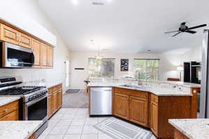 Kitchen featuring appliances with stainless steel finishes, light tile patterned flooring, light stone countertops, pendant lighting, and brown cabinetry