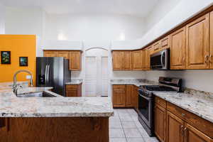 Kitchen with stainless steel appliances, brown cabinetry, light stone countertops, and a towering ceiling